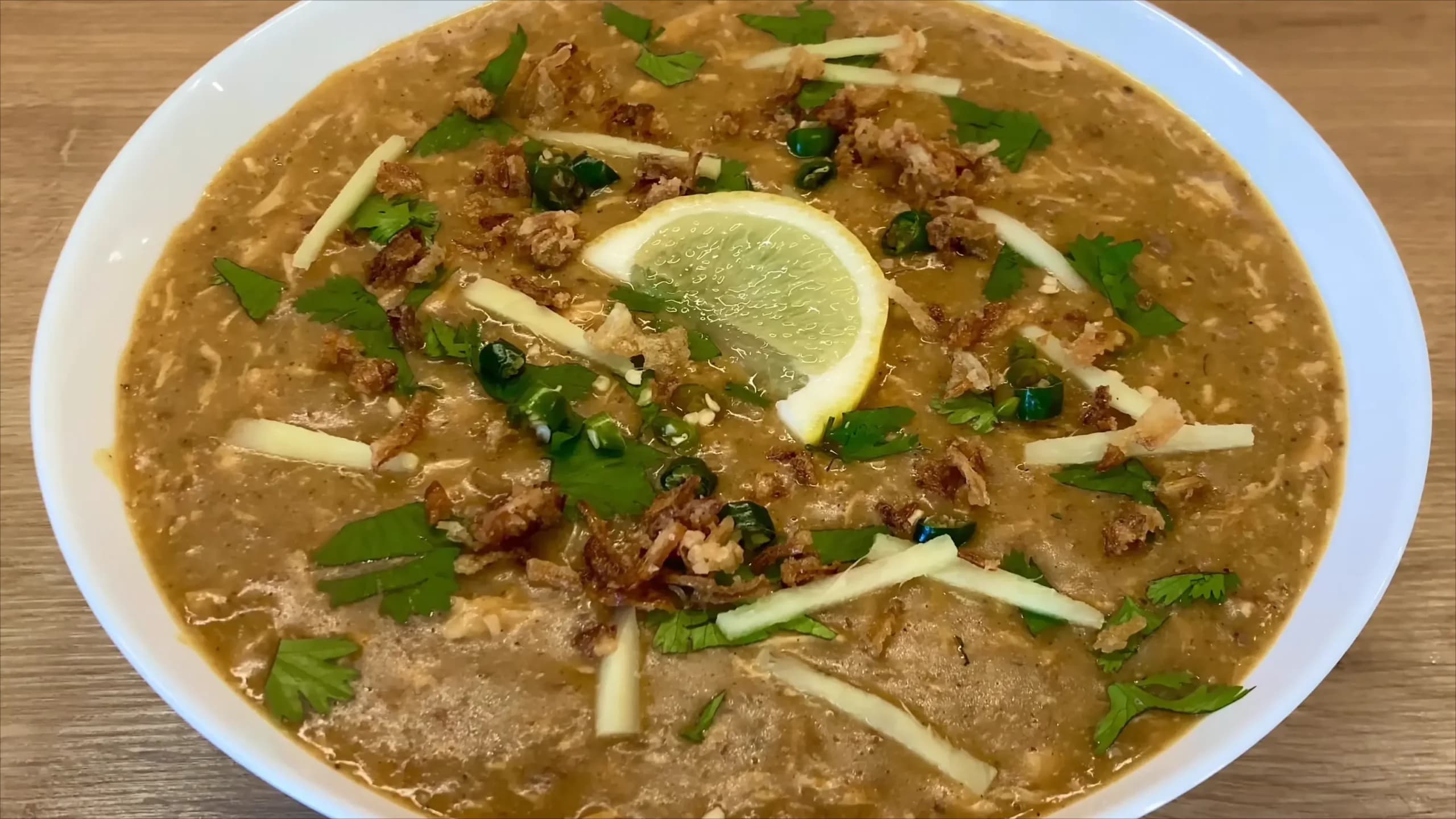 A bowl of Haleem garnished with fried onions, ginger, and lemon